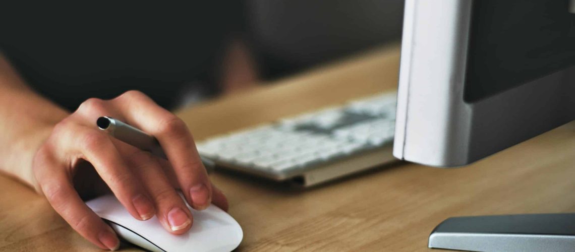 Free A hand using a wireless mouse at a modern desk setup with a computer and keyboard. Stock Photo