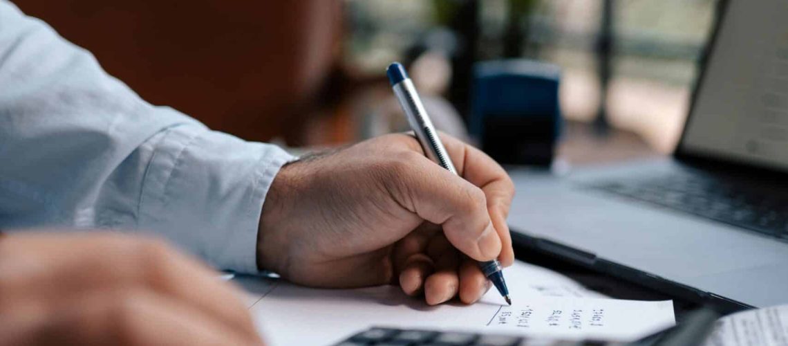 Free A person calculating finances with a calculator and pen on a desk indoors. Stock Photo